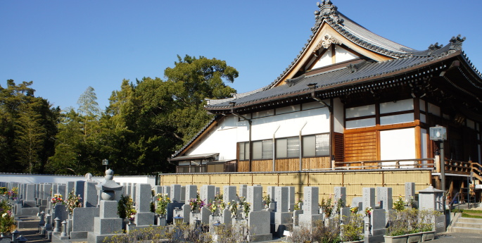 青空の下に佇む寺院の屋根と、整然と並ぶ墓地の風景