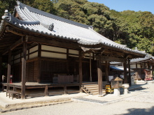 豊かな木々を背に建つ、伝統的な日本建築の寺院本堂の外観