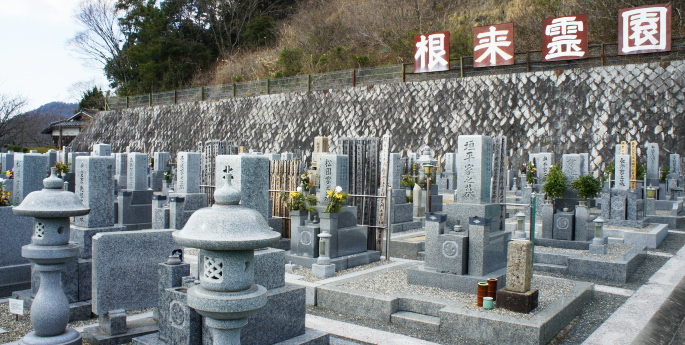 「根来霊園」の大きな看板が掲げられた、石壁沿いに並ぶ和型墓石群