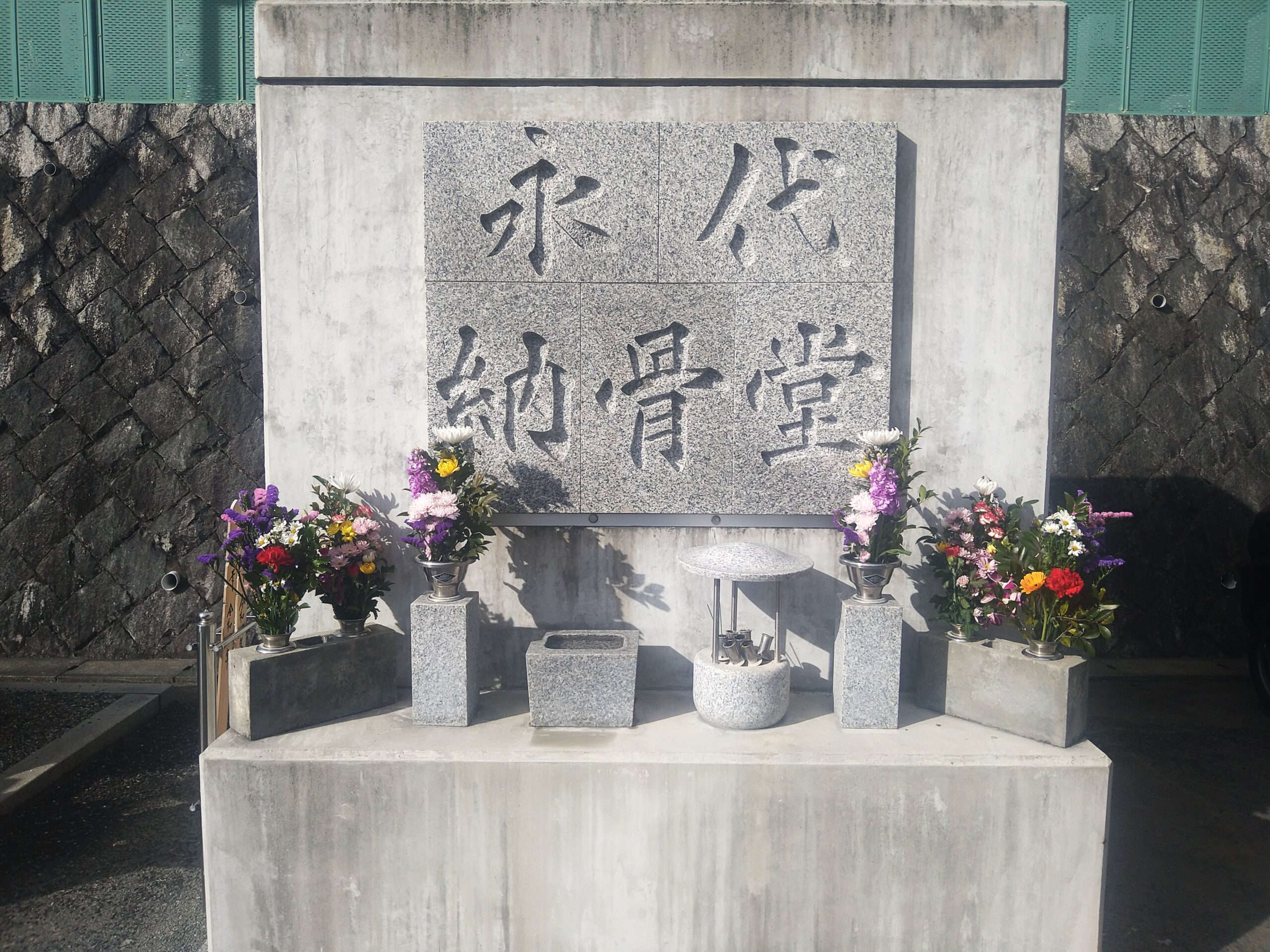 「永代納骨堂」と刻まれた石碑と供えられた色鮮やかな花
