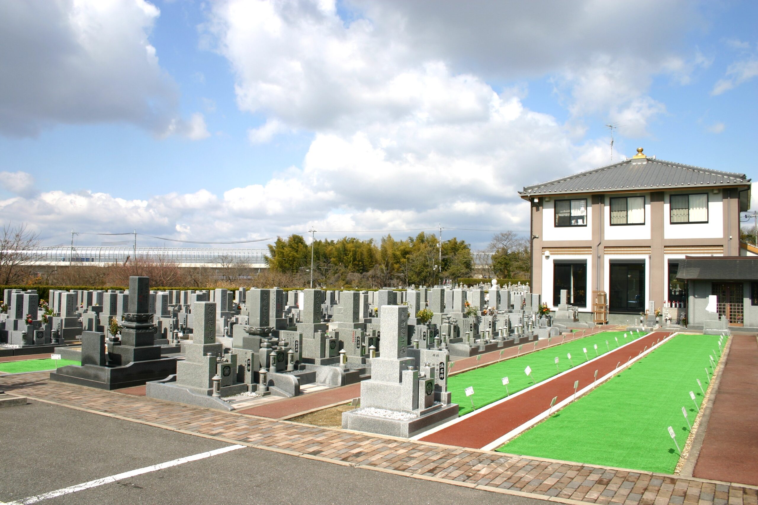 青空の下に広がる章園寺の整然とした墓地と2階建ての白い管理棟