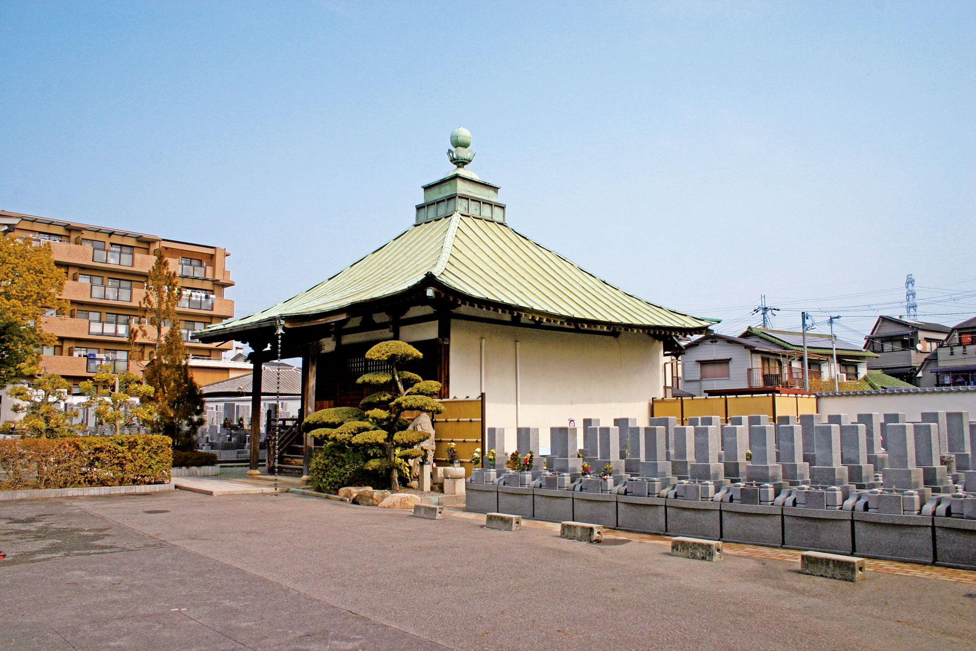 銅板葺きの屋根が特徴的な寺院の建物と、手前に並ぶ石造りの墓石
