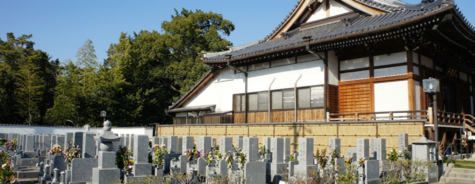 青空の下に広がる寺院の本堂と整然と並ぶ墓石の風景
