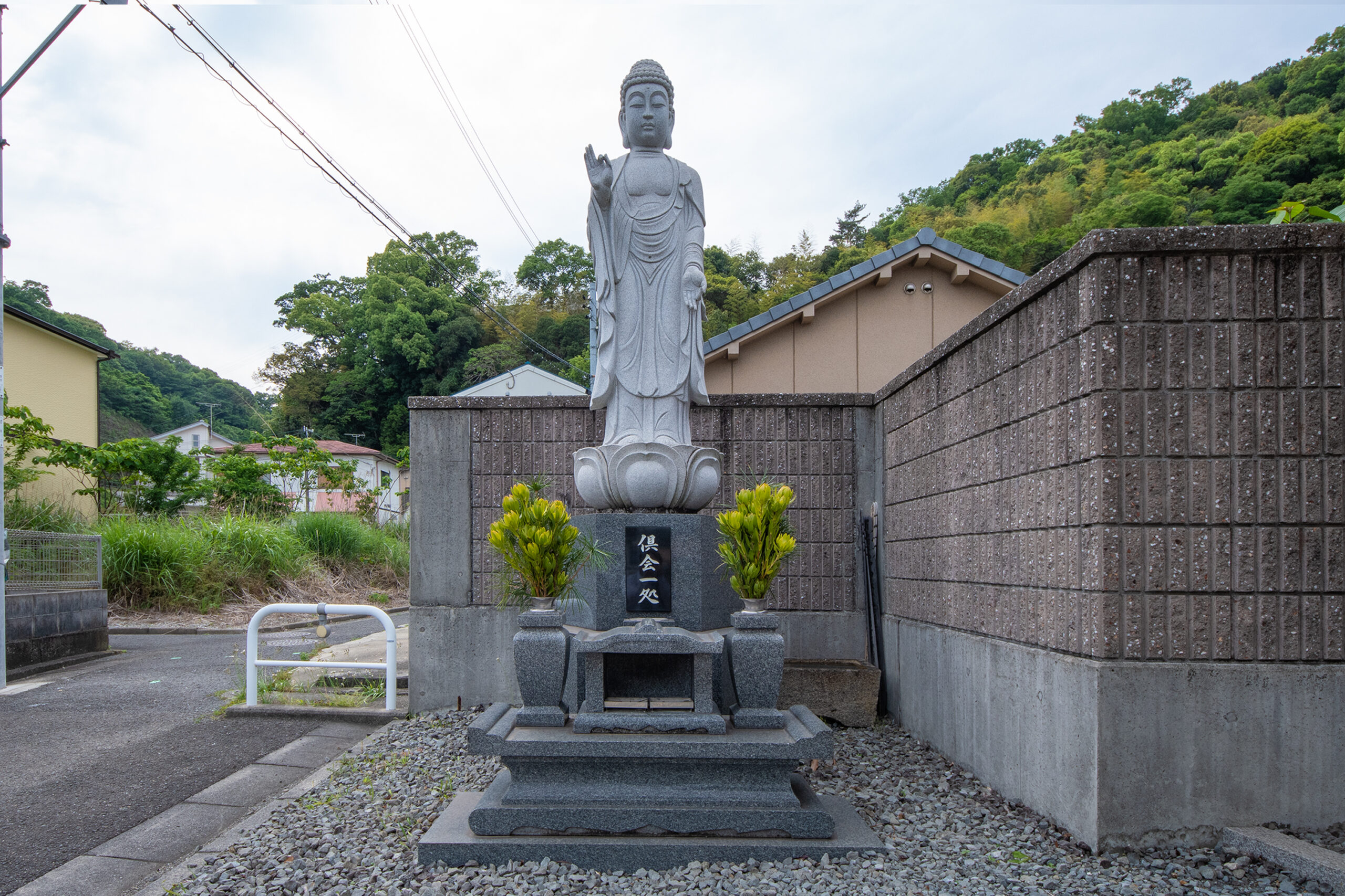 青空と緑の山を背景に立つ、穏やかな表情をした石造りの聖観音菩薩像