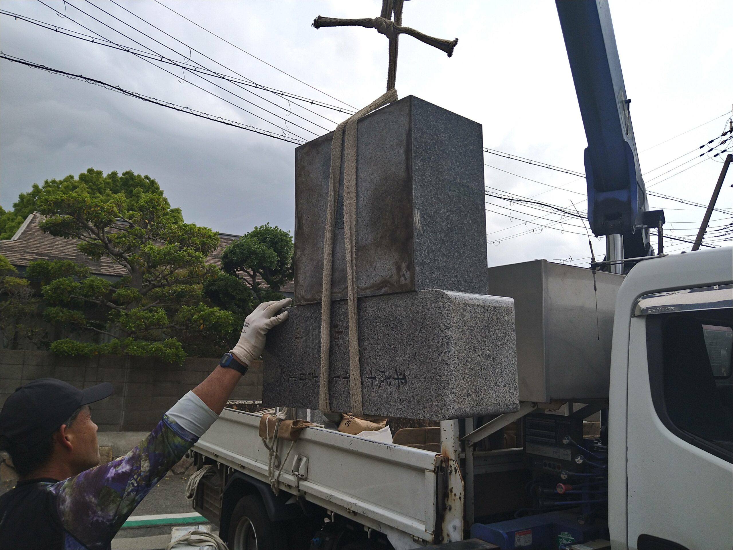 クレーン車を使用して、トラックの荷台から大きな墓石を吊り上げる様子
